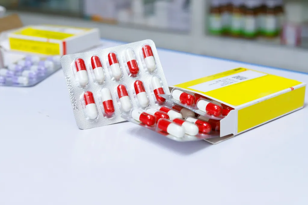 Capsules in foil strips beside an open medicine box on a pharmacy counter